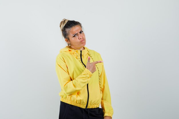 Femme en costume de sport pointant vers le côté et regardant sombre, vue de face.