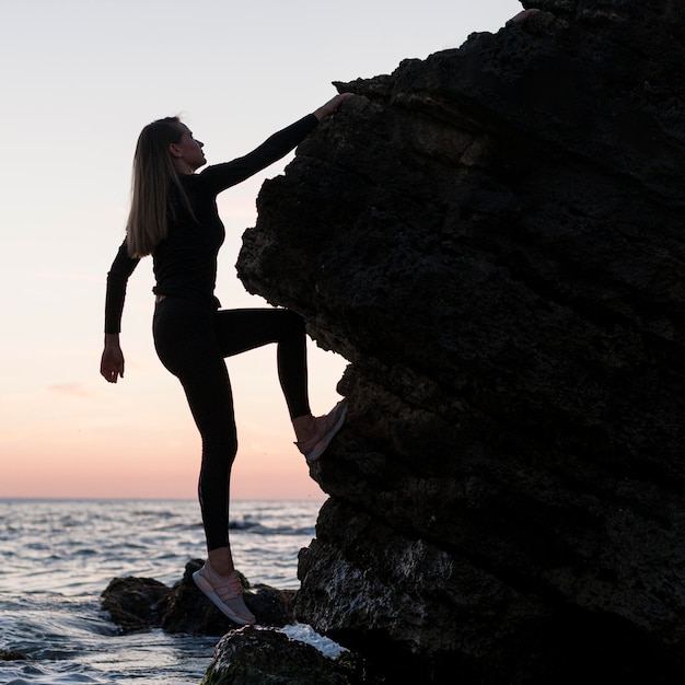 Femme sur le côté escalade un rocher à côté de l'océan