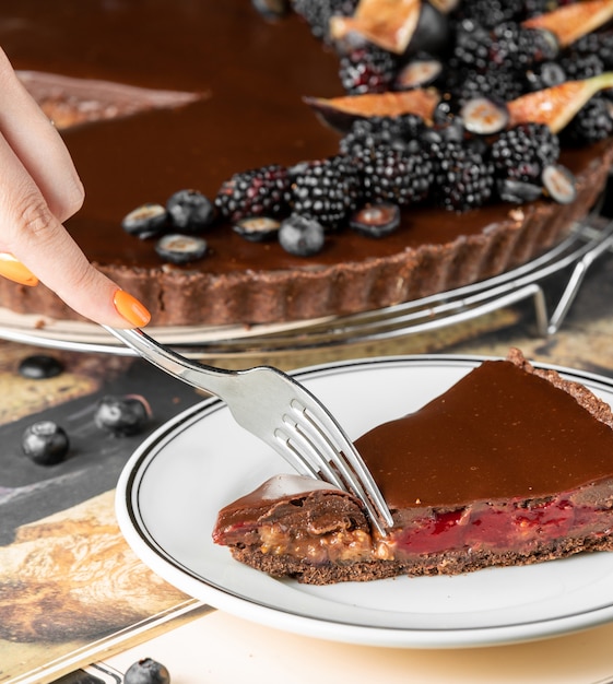 Photo gratuite femme coupant un morceau de gâteau au fromage au chocolat avec framboises et noix