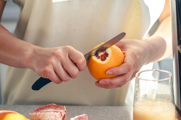 Photo gratuite une femme coupe une orange dans la cuisine et fait du jus dans un juicer