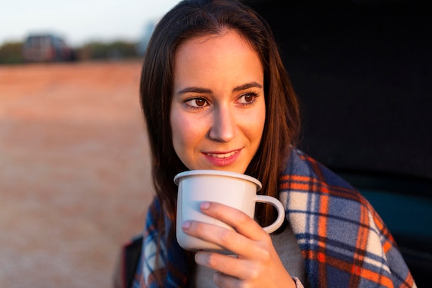 Femme avec couverture sur boire du café tout en admirant le coucher du soleil