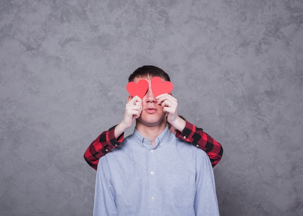 Femme, couvrant, yeux homme, à, papier rouge, coeurs