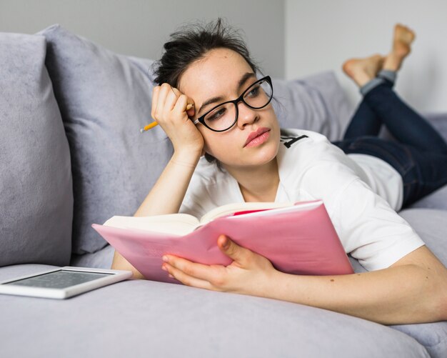 Femme avec un crayon et un livre allongé sur le canapé