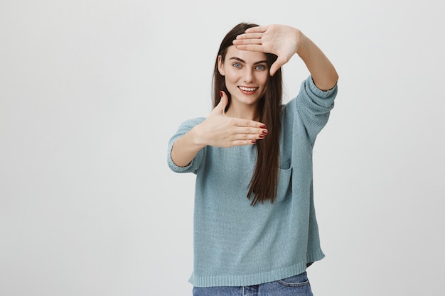 Femme créative souriante faisant des mains de cadre, s'inspirant