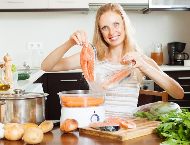 Femme cuisinant des légumes et du saumon avec un steamer électrique