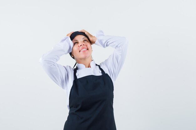 Femme cuisinier en uniforme, tablier tenant les mains sur la tête et à la vue de face, heureux.