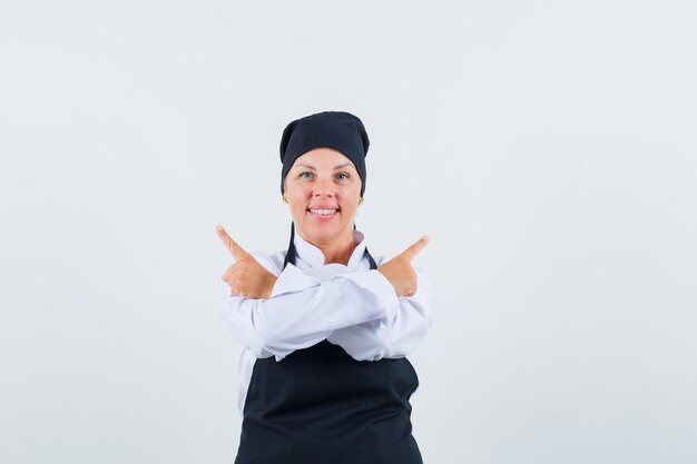 Femme cuisinière pointant vers l'extérieur en uniforme, tablier et l'air confiant. vue de face.