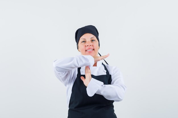 Femme cuisinière en uniforme, tablier montrant le geste de pause et à la confiance, vue de face.