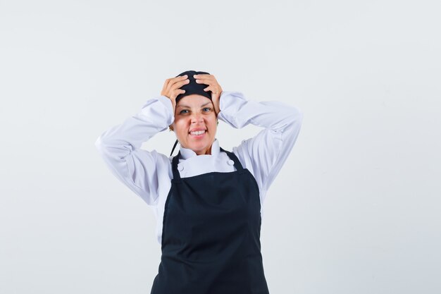 Femme cuisinière en uniforme, tablier tenant les mains sur la tête et à la vue de face, oublieux.