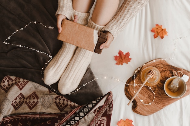 Femme de culture avec barre de chocolat près de miel et de thé