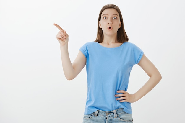 Femme curieuse et intriguée pointant le coin supérieur gauche intéressé par le logo ou l'offre promotionnelle