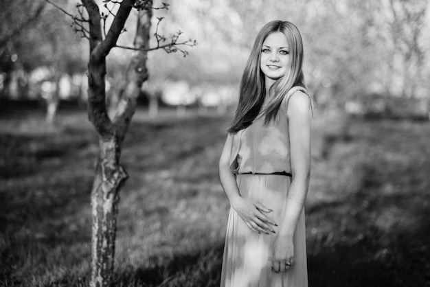 Femme dans une belle longue robe turquoise posant sur un pré dans le jardin fruitier