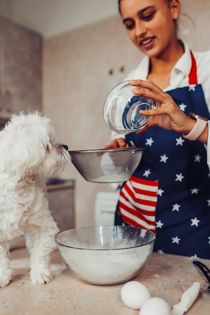 Photo gratuite femme dans la cuisine tamise la farine avec un chien