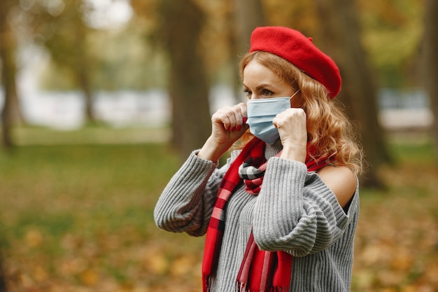 Femme dans la forêt d'automne. Personne dans un masque. Thème du coronavirus. Dame dans un foulard rouge.