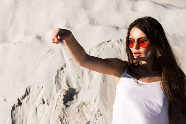 La femme dans les lunettes de soleil rouges se trouve sur une plage blanche