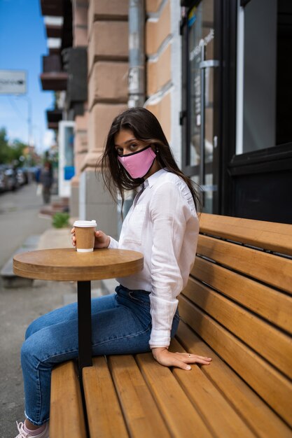 Femme dans un masque médical boit du café dans la rue