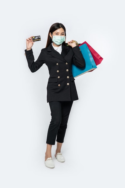 Une femme dans le noir et portant un masque se promène dans les magasins, porte des cartes de crédit et beaucoup de sacs