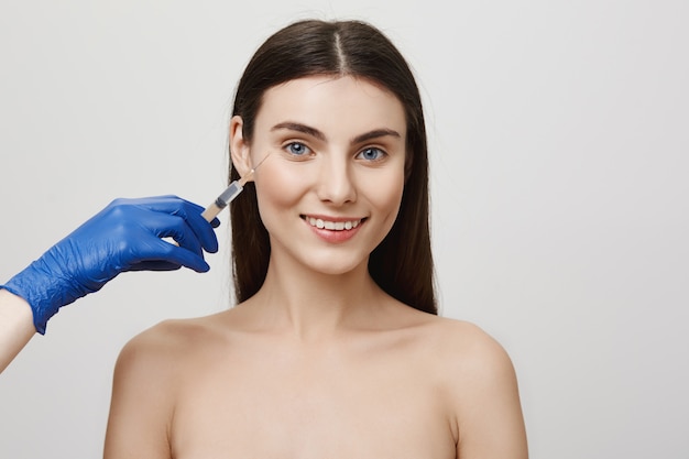 Femme dans un salon de beauté souriant joyeux, recevoir une injection de visage bottox avec une seringue