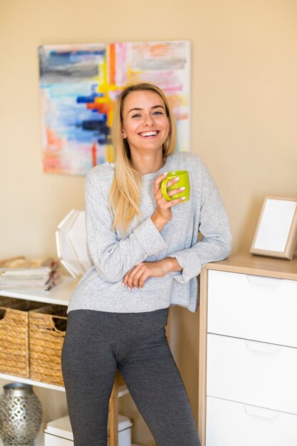 Femme dans le salon sourit et tient une tasse