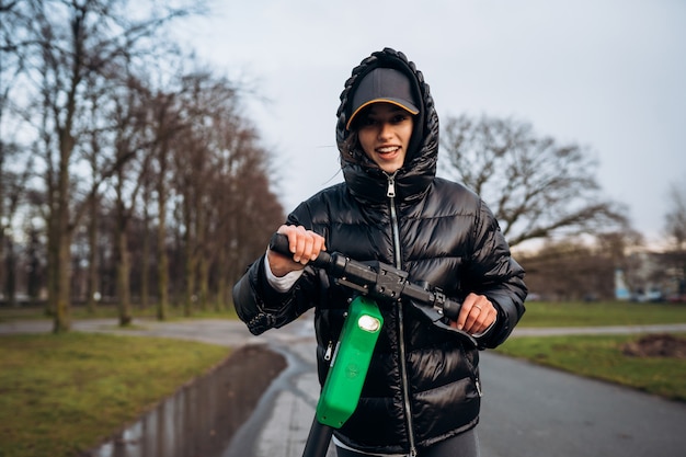 Femme dans une veste sur un scooter électrique dans un parc en automne.