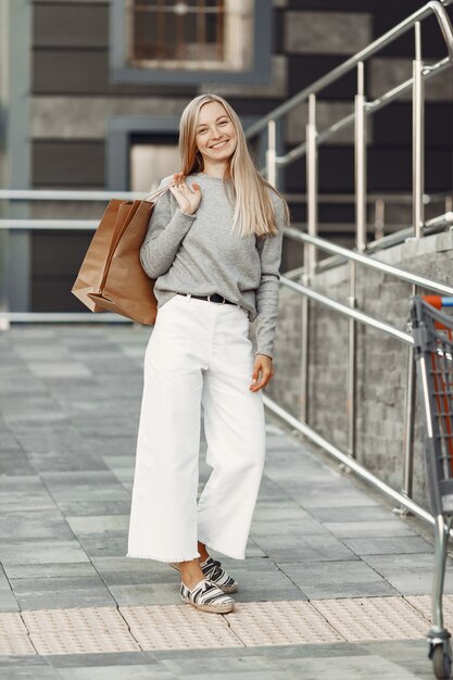 Femme dans une ville d'été. Dame aux sacs marron. Femme dans un pull gris.