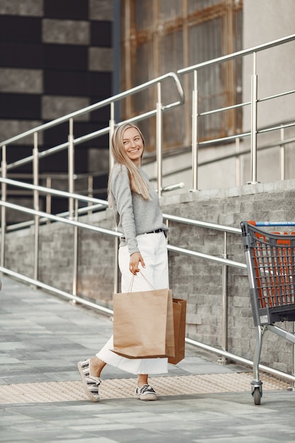 Femme dans une ville d'été. Dame aux sacs marron. Femme dans un pull gris.