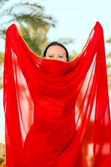 Une femme une danseuse orientale sur fond de palmiers avec une cape fermée son visage