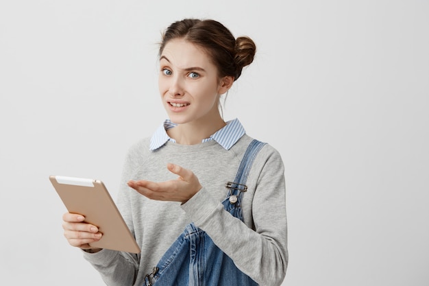 Femme debout avec un air bouleversé indiquant que sa tablette dorée est hors service. Malheureuse cliente se plaignant d'un gadget inopérant acheté en boutique. Technique, fonctionnalité