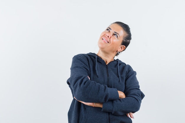 Femme debout avec les bras croisés à capuche et à la rêveuse, vue de face.