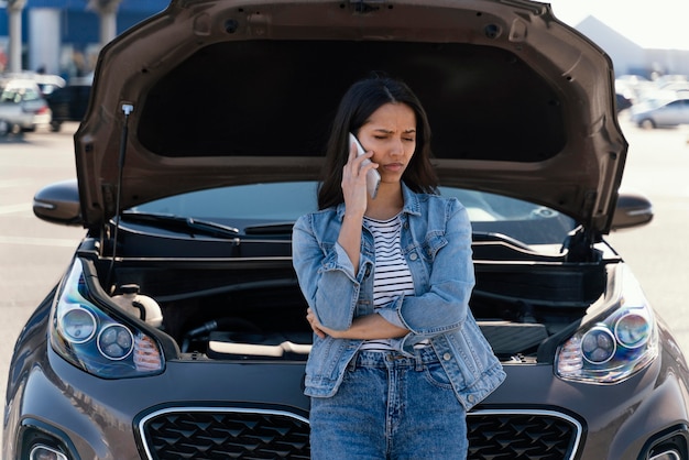 Femme debout à côté de sa voiture cassée