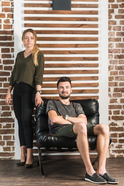 Femme debout à côté de son petit ami assis sur une chaise confortable