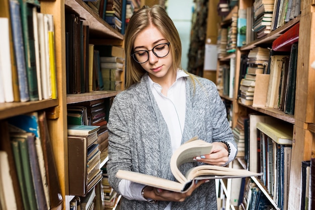 Femme debout entre les bibliothèques et tourner les pages du livre