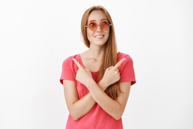 Femme debout entre deux choix ayant des doutes sur ce qu'il y a de mieux en pointant de différents côtés avec les mains croisées sur la poitrine à droite et souriante comme si elle avait décidé de l'affaire à prendre