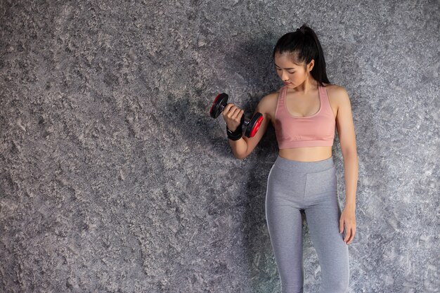 Femme debout exerçant avec un haltère rouge dans la salle de gym.