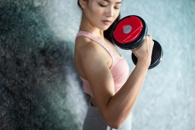 Femme debout exerçant avec un haltère rouge dans la salle de gym.