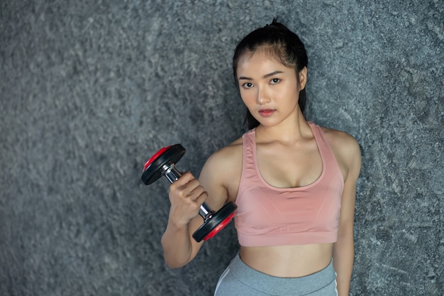 Femme debout exerçant avec un haltère rouge dans la salle de gym.