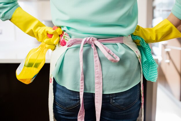 Femme debout avec flacon pulvérisateur et serviette dans la cuisine