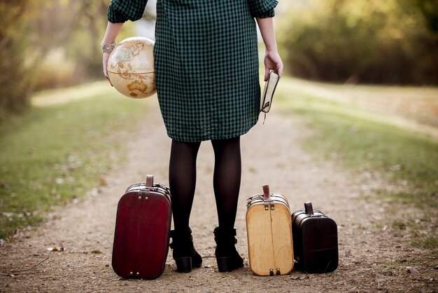 Femme debout sur une route vide près de sa valise tout en tenant la bible et un globe