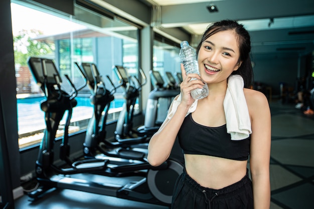 Femme debout et se détendre après l'exercice, tenant une bouteille d'eau pour toucher le visage.