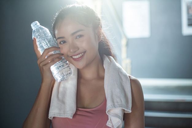 Femme debout et se détendre après l'exercice, tenant une bouteille d'eau pour toucher le visage.