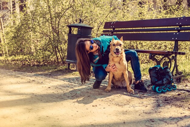 Femme décontractée souriante avec son chien pitbull brun dans un parc.