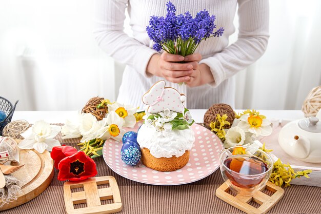 Une femme décore une table avec des friandises de labour avec des fleurs. Concept de vacances de Pâques.