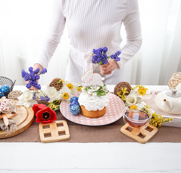 Une femme décore une table avec des friandises de labour avec des fleurs. Concept de vacances de Pâques.