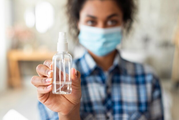 Femme défocalisée avec masque médical tenant un désinfectant pour les mains