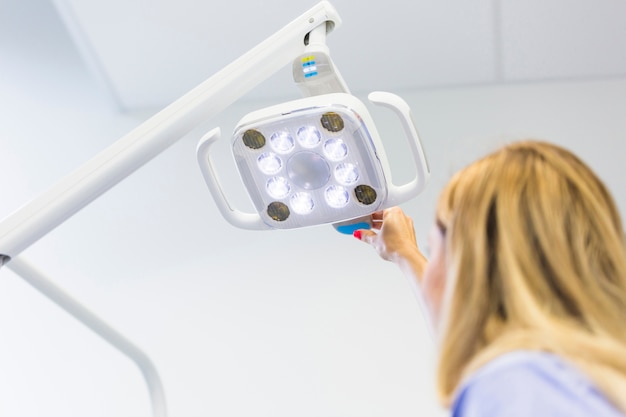 Femme dentiste ajustant une lampe médicale en clinique