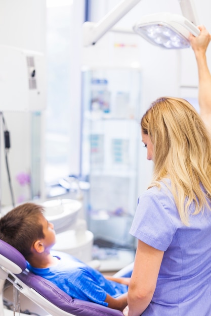 Femme dentiste debout près de garçon assis sur une chaise dentaire