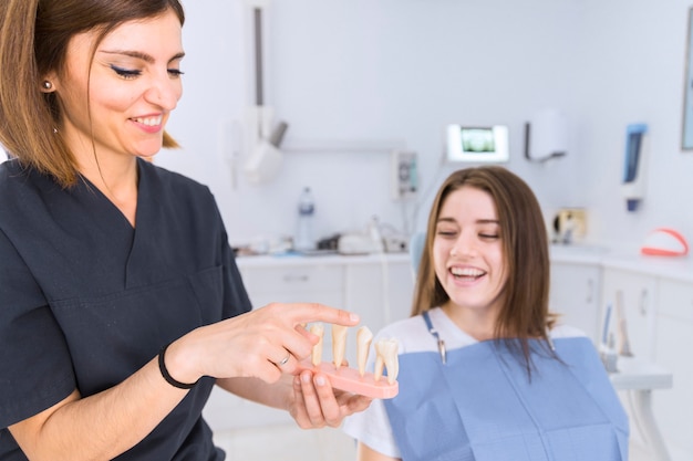 Photo gratuite femme dentiste montrant le modèle de dents à une patiente à la clinique dentaire