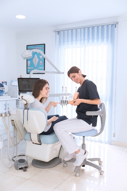 Femme dentiste montrant le modèle de dents à sourire patient en clinique