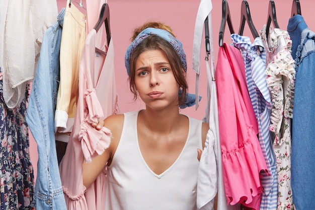 Femme déprimée debout près d'une armoire pleine de vêtements, ayant un choix difficile ne sachant pas quoi mettre.