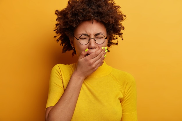 Photo gratuite une femme déprimée à la peau sombre pleure de désespoir, se couvre la bouche, a l'air misérable, gémit bruyamment, porte des lunettes optiques, un t-shirt décontracté jaune, pose à l'intérieur, fatiguée des problèmes. émotions négatives